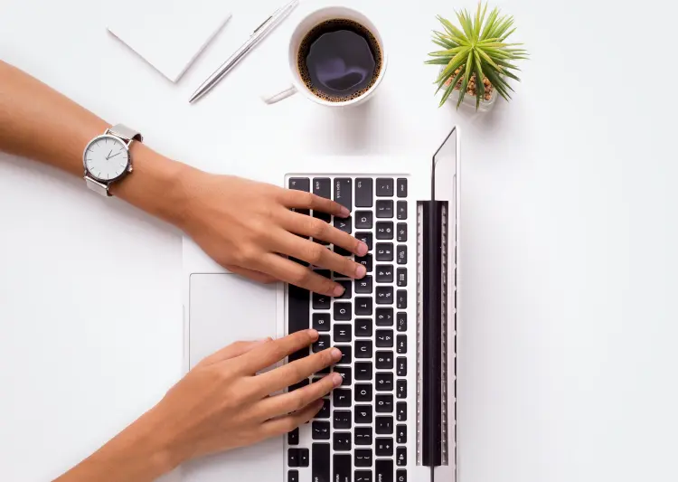 Person typing on laptop with coffee